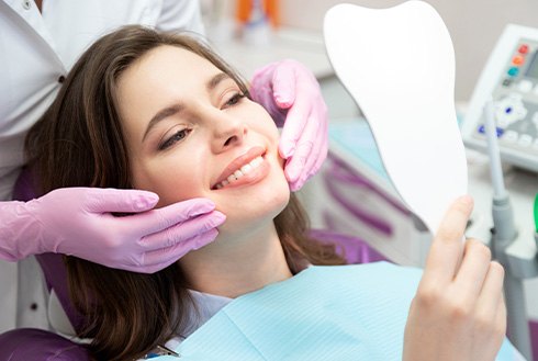 Woman in dental chair smiling at reflection in handheld mirror