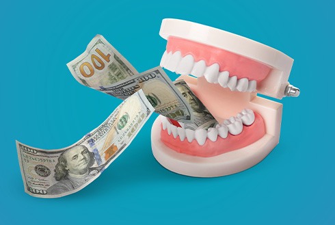 Artificial teeth chomping dollar bills with light blue background