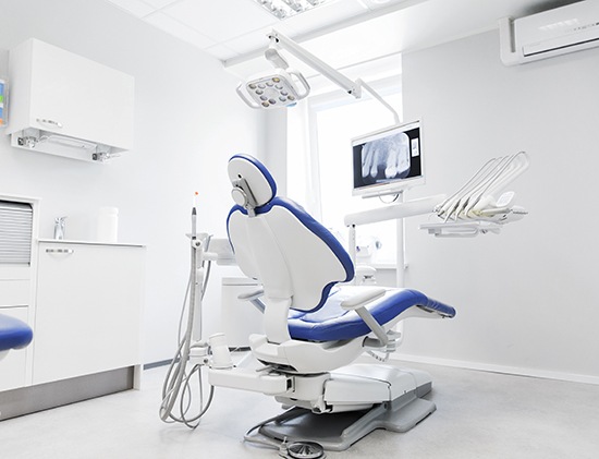 Blue dental chair in a white examination room with x-ray displayed on a monitor