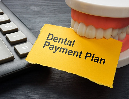 Artificial teeth clamped on a yellow paper that says Dental Payment Plan