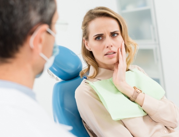 Woman holding cheek in pain while talking to emergency dentist