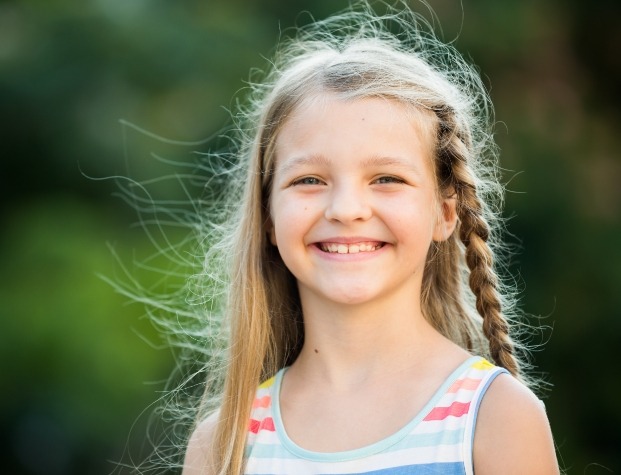 Young blonde girl with braid grinning outdoors