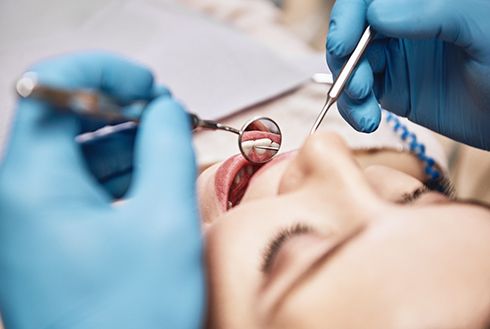 Facial closeup of a woman undergoing an oral exam by a dentist with blue gloves