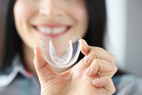 Woman blurry in the background holding a clear mouthguard to the foreground 