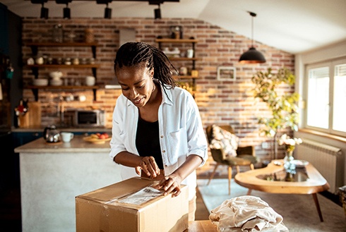 Woman wearing black and white shirts opening a box in a room with a brick wall